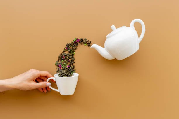 Female hand pours tea leaves from teapot in cup.